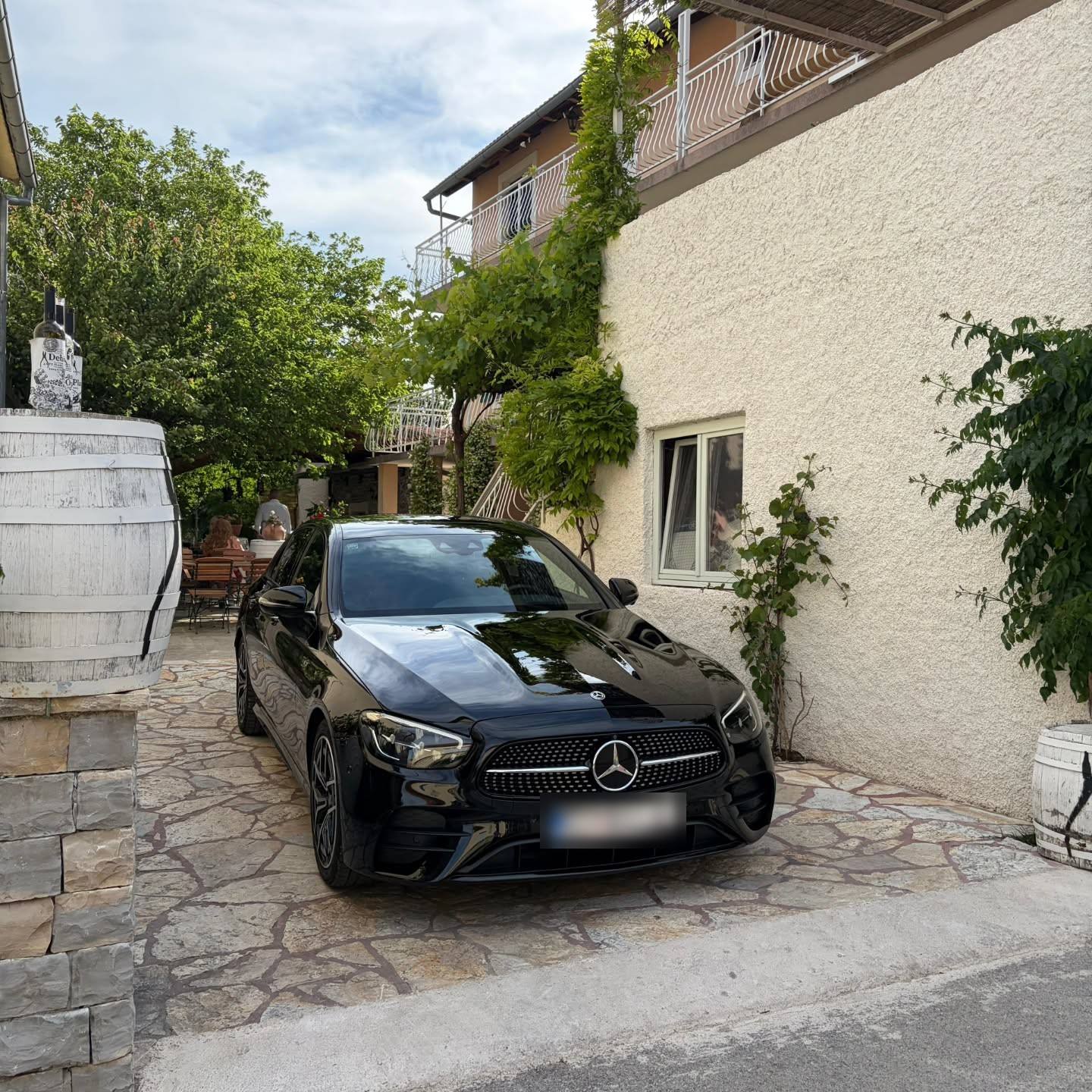 A black car parked on stone paving beside a house covered in vines
